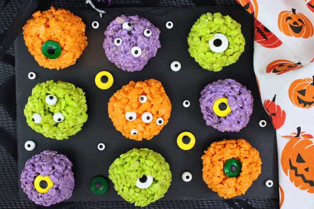 overhead view of colorful monster rice krispie treats with various candy eyes on slate nex to halloween napkin