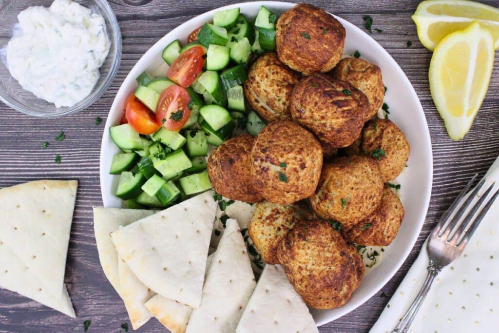 overhead view of trader joes turkey meatballs on a plate with diced cucumbers, tomatoes, and pita wedges