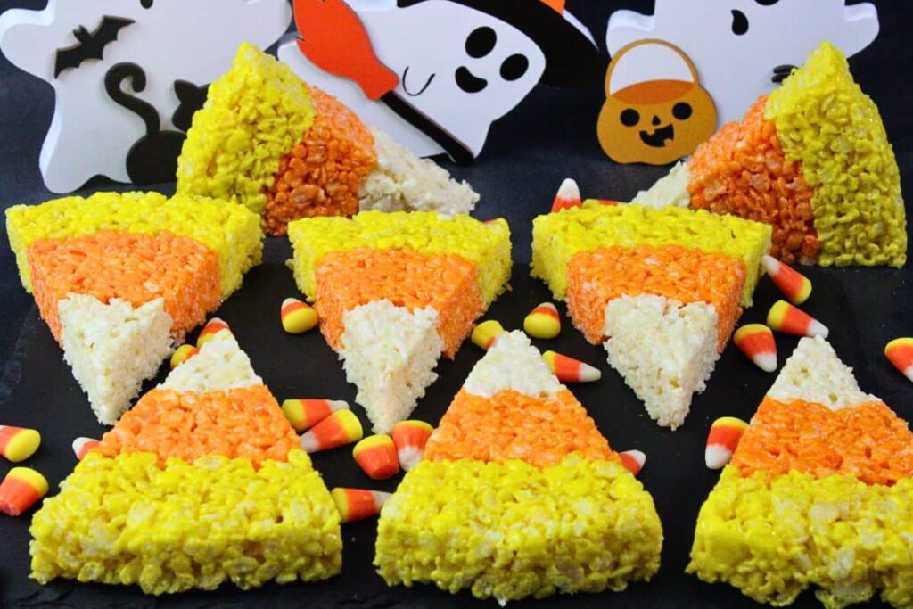 several candy corn rice krispie treats on black slate surrounded by candy