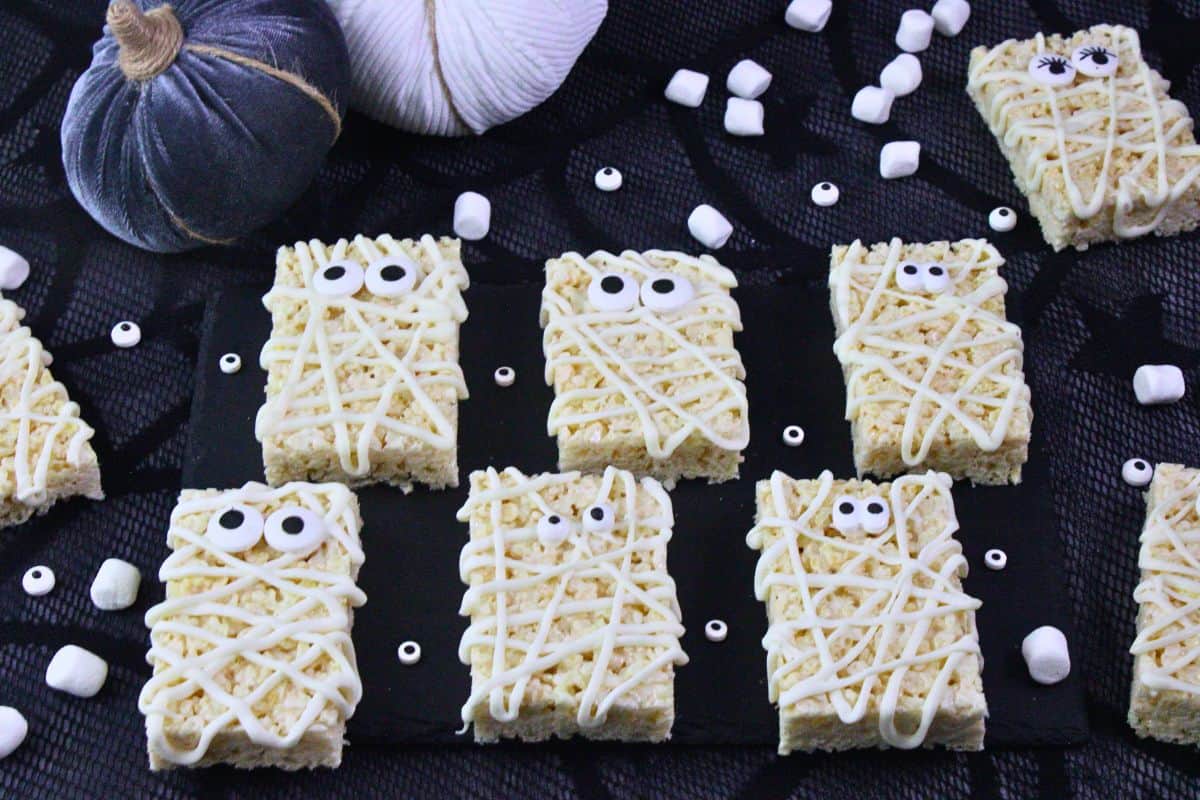 several mummy rice krispie treats with candy eyes laying on slate on top of webbed mat