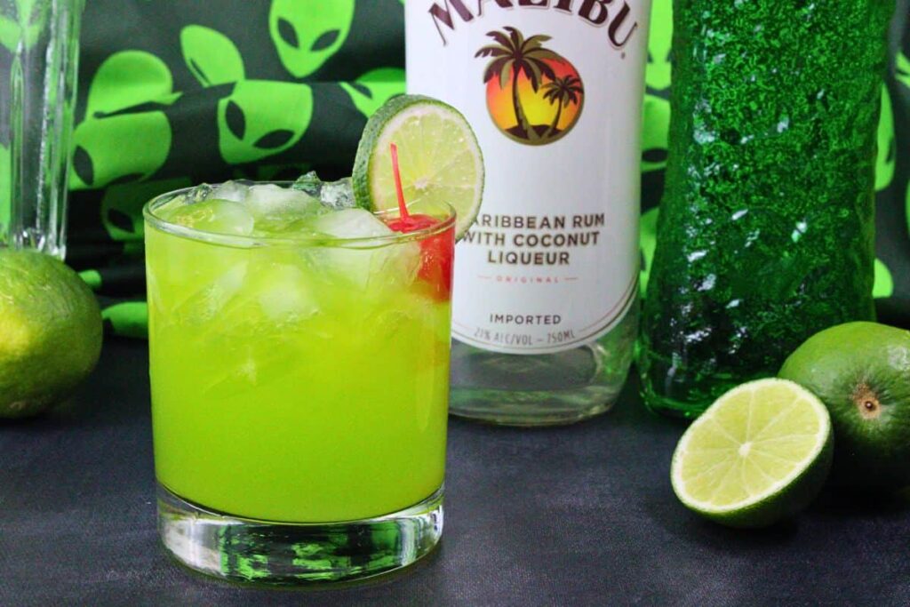 alien secretion drink with lime wheel and cherry in front of liquor bottles