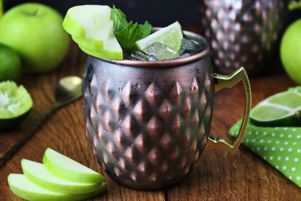 closeup of crown apple mule in copper mug with apple, lime, and mint garnish