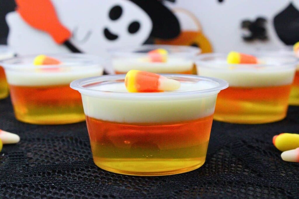 closeup view of layered candy corn jello shots in front of halloween ghosts