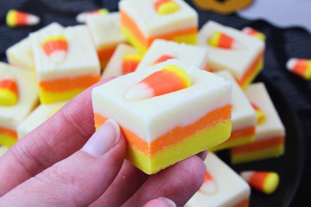 holding up a square of layered candy corn fudge with candy on top