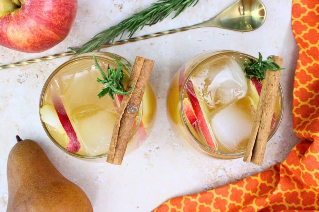 overhad view of two apple cider sangria glasses topped with apple and pear slices, cinnamon, and rosemary