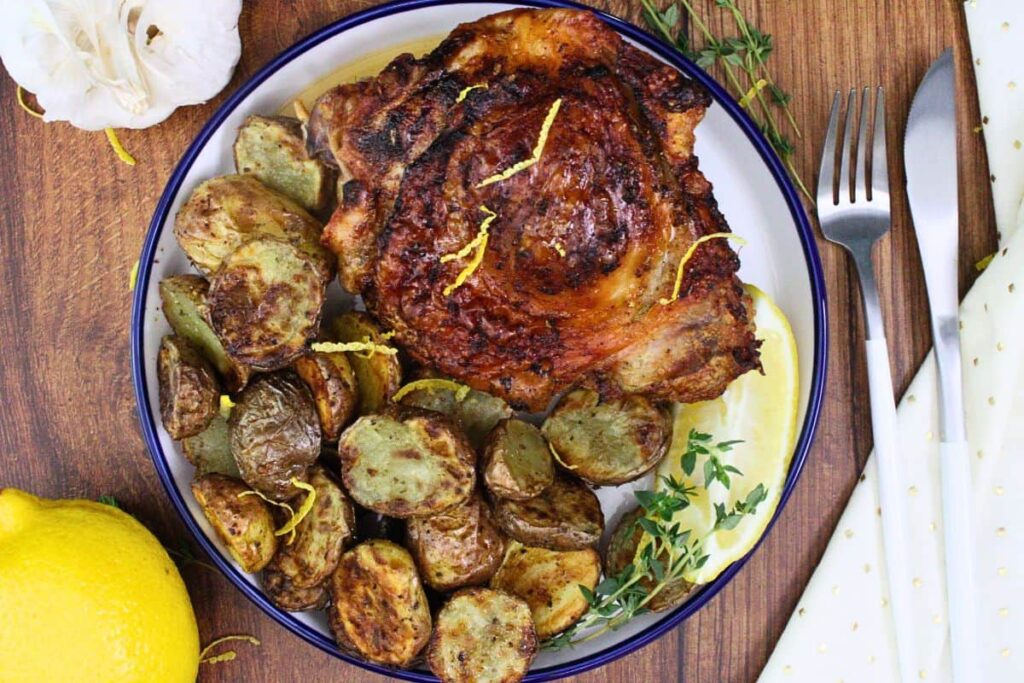overhead view of crispy air fryer turkey thigh on a plate with potatoes and herb garnish