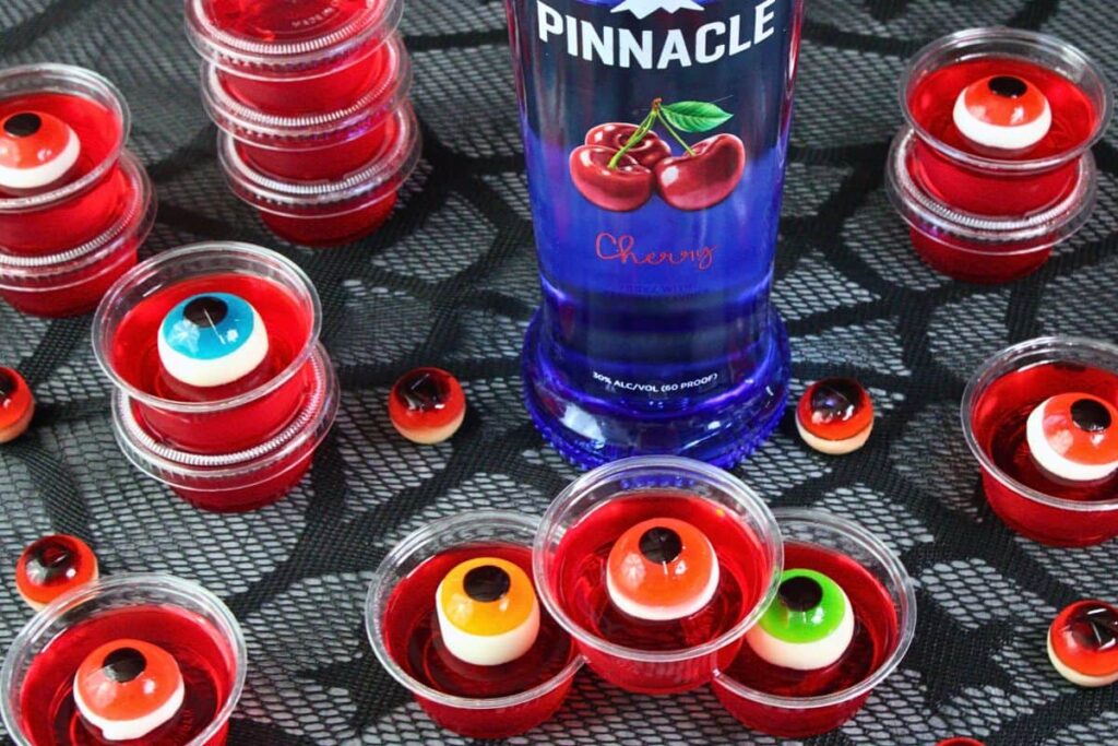 overhead view of eyeball jello shots scattered and stacked around a vodka bottle on black web lace mat