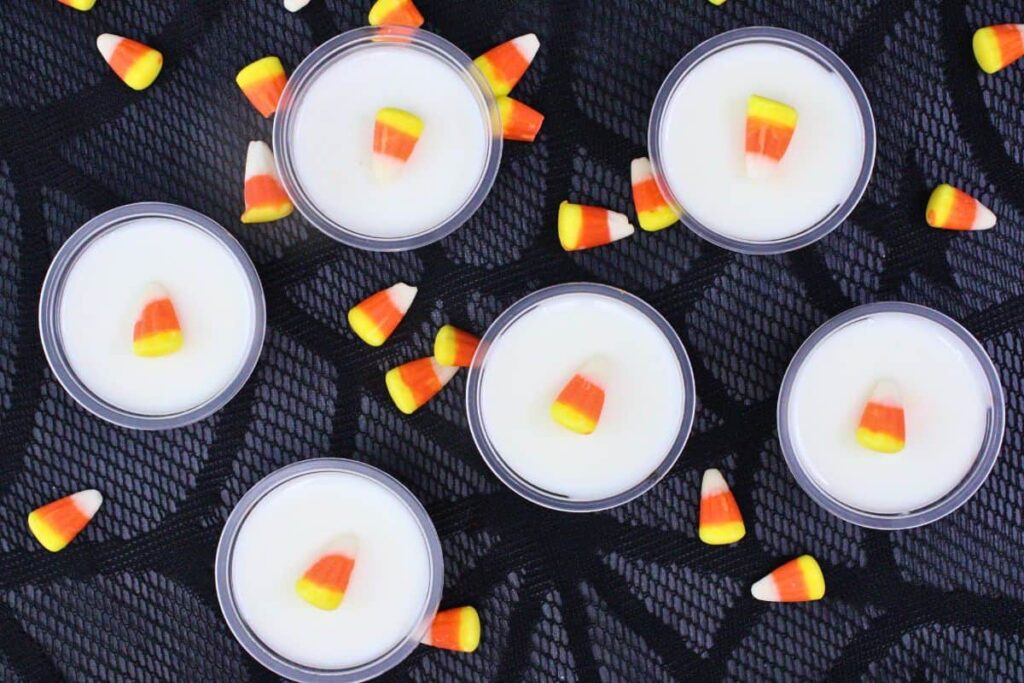overhead view of several candy corn jello shots topped with candy on a halloween web mat