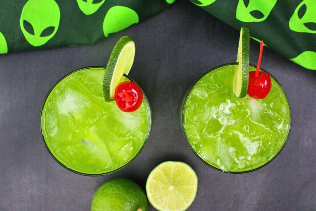 overhead view of two alien secretion drinks with lime and cherry garnish on black counter