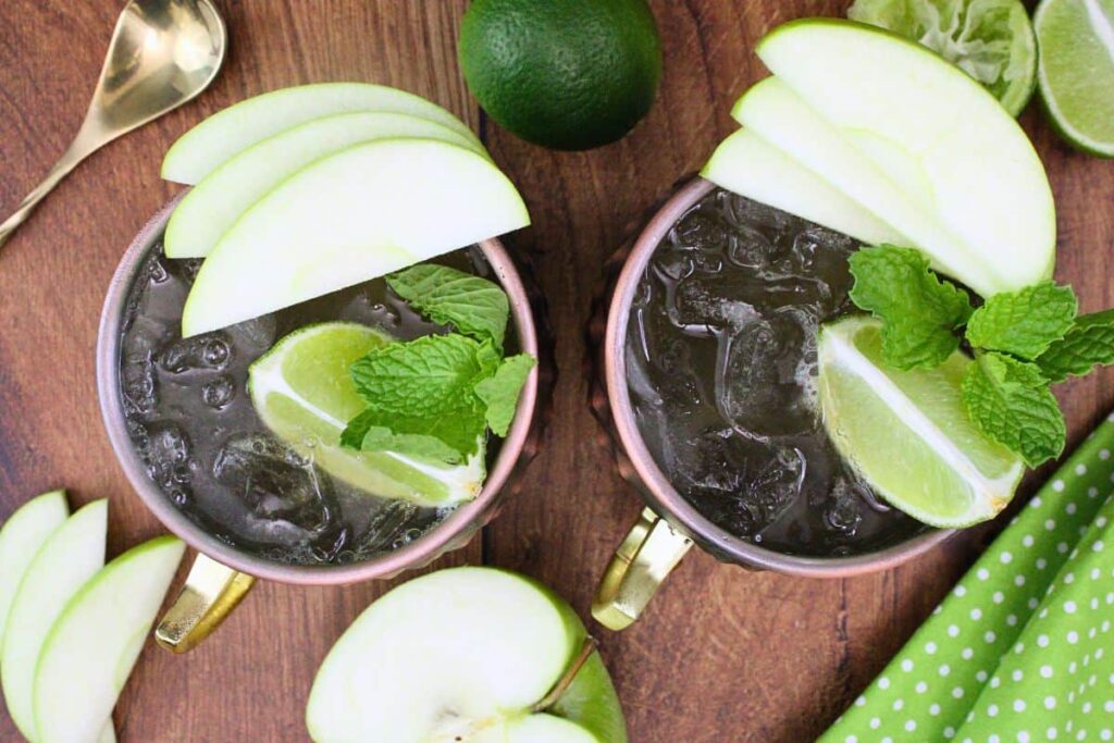 overhead view of two crown apple mule drinks in copper mugs with apple slices, lime, and mint garnish