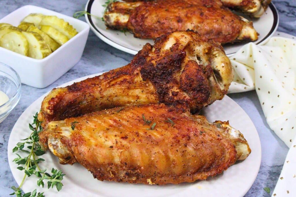 two air fryer turkey wings on a plate with thyme showing off their crispy skin
