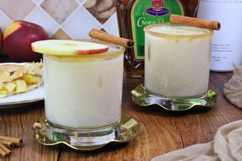 two apple pie cocktails on coasters with apple slice and cinnamon stick garnish