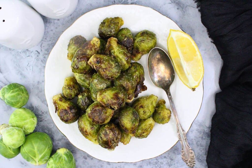 over head view of air fryer frozen brussel sprouts on a plate next to a spoon and lemon wedge
