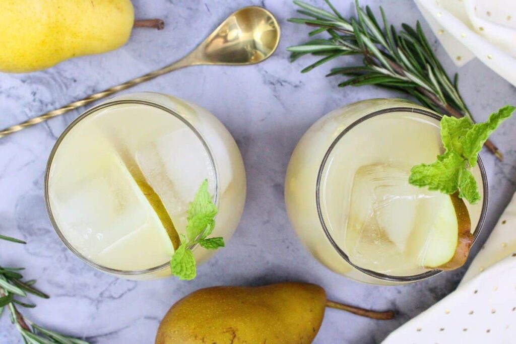 overhead view of two pear spritz cocktails garnished with pear slices and mint surrounded by fresh fruit and rosemary