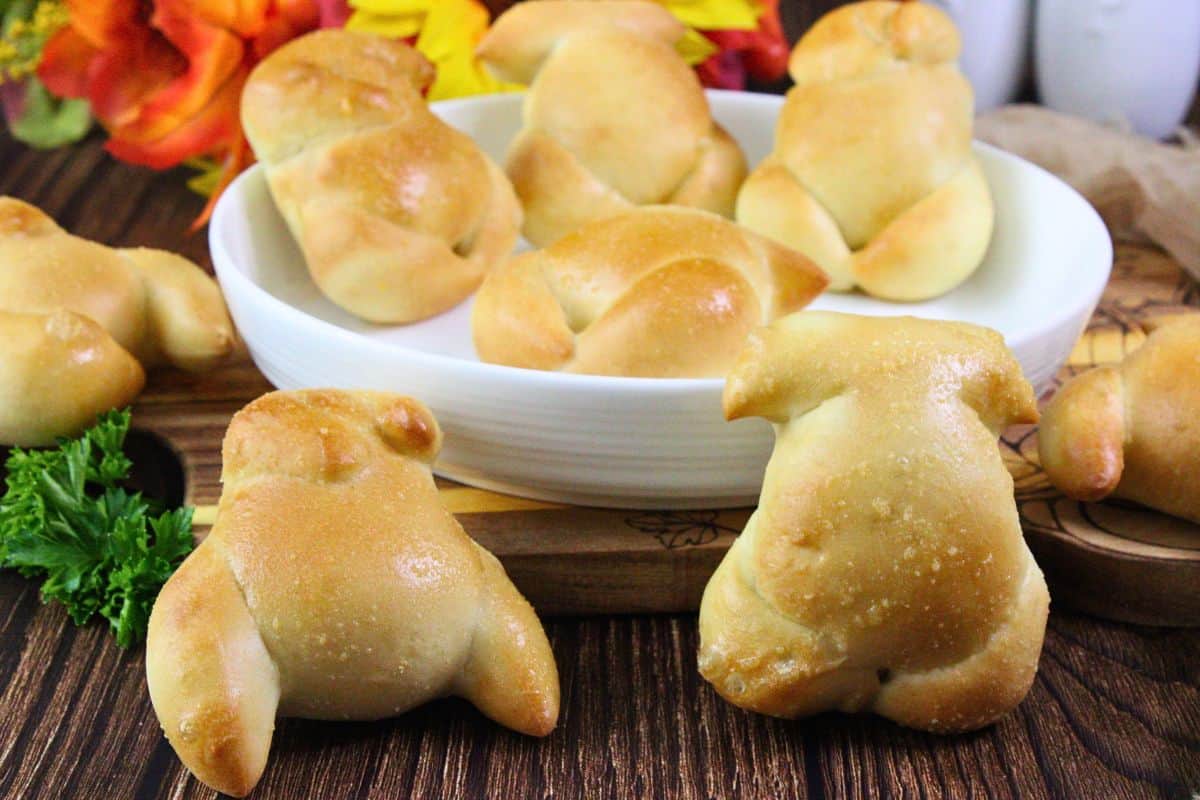 several air fryer turkey dinner rolls sitting on a wooden table with parsley and more in a white bowl