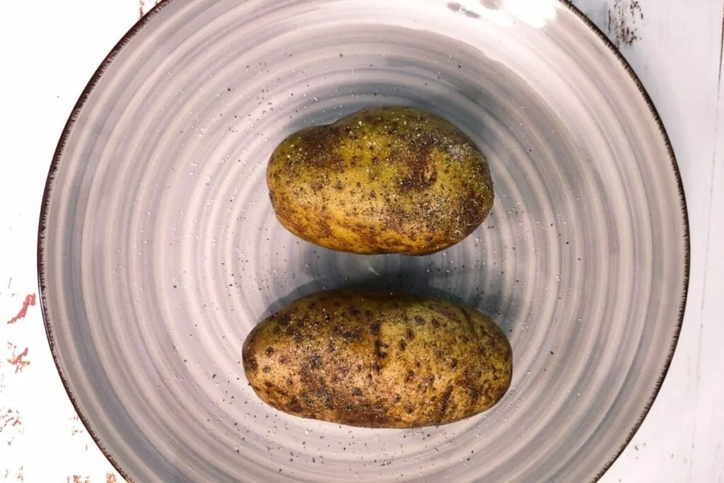 2 russet potatoes on plate with olive oil and salt and pepper