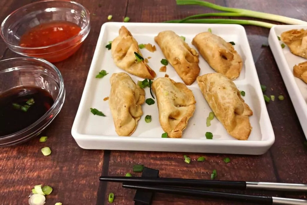 golden brown crab rangoons on a square plate in two rows of three with soy and duck sauce on the side