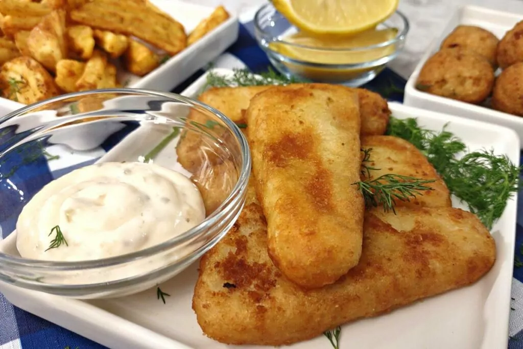 crunchy fish fillet with tartar sauce and side dishes in the background