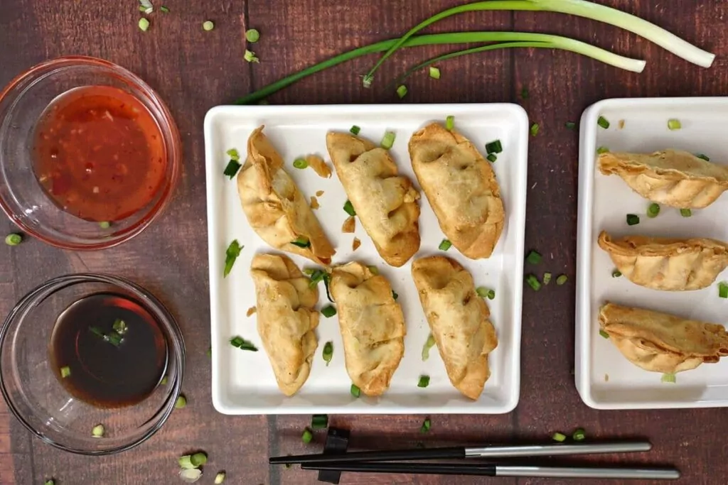 overhead view of six crab rangoons on a plate with soy sauce and duck sauce to the left