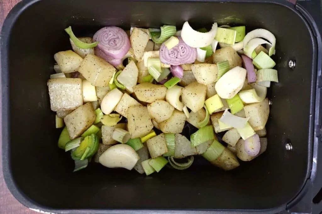 add shallots, leeks, and garlic cloves to the potatoes in air fryer basket