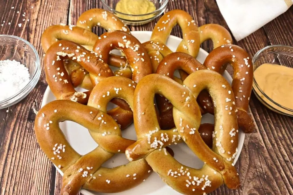 air fryer soft pretzels on a plate with salt, mustard, and cheese sauce on the side
