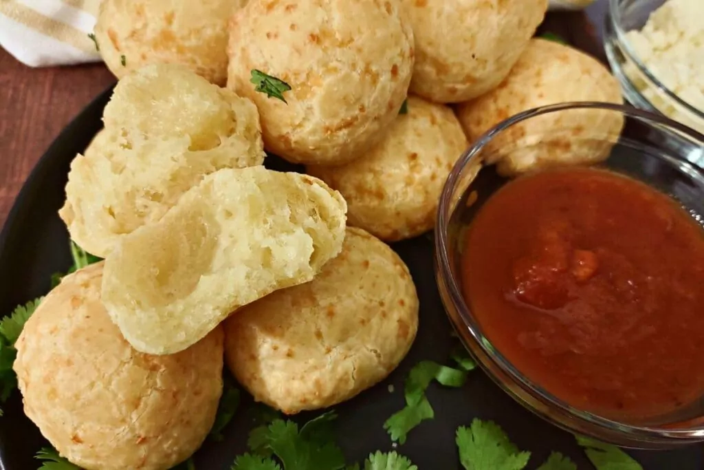 brazilian cheese bread staked on a plate with marinara and cheesy cross section
