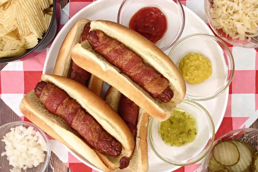 overhead view of air fryer bacon wrapped hot dogs on a plate with ketchup and mustard
