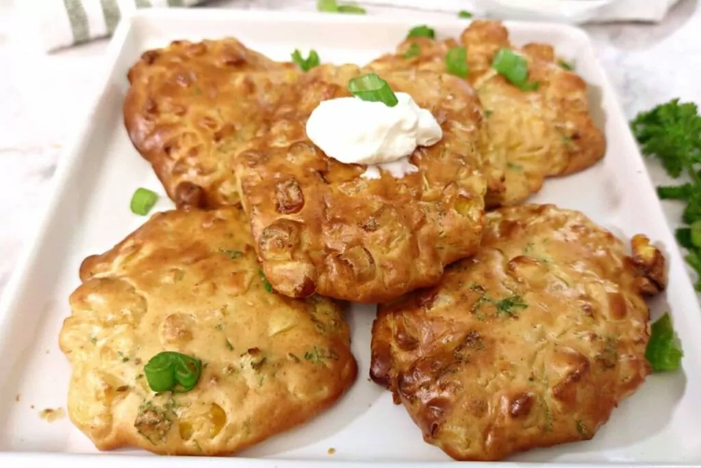 air fryer corn fritters stacked up with sour cream on top