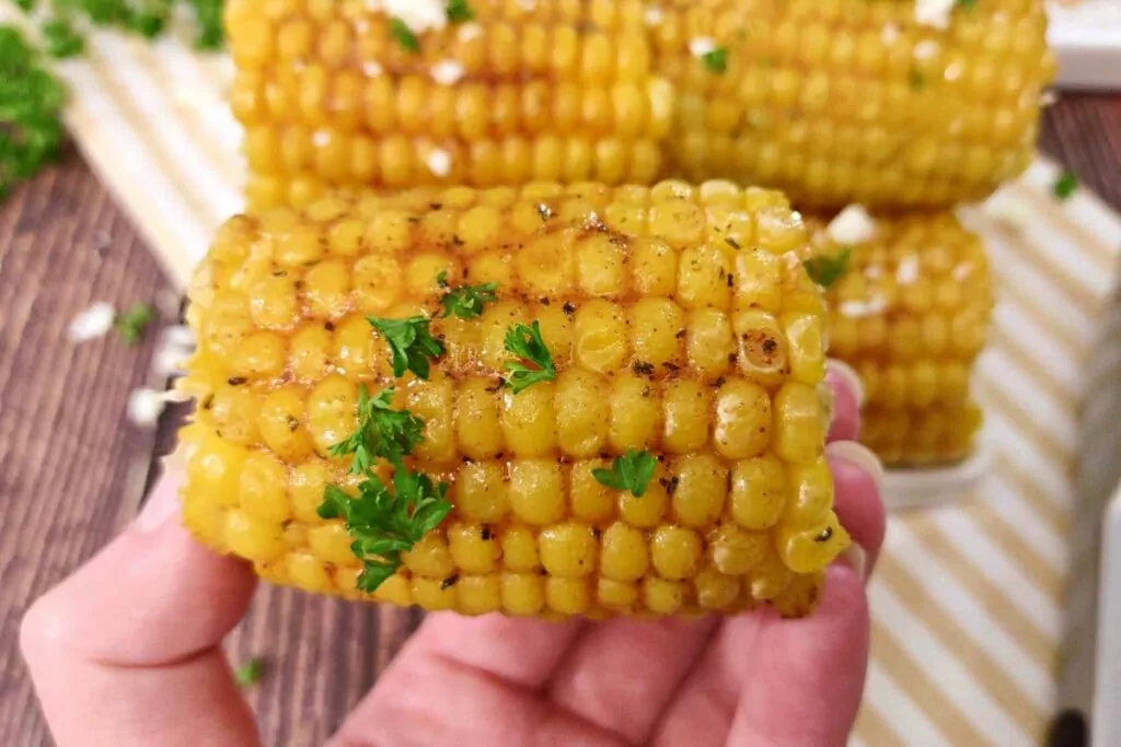 holding a piece of buttered air fryer corn on the cob