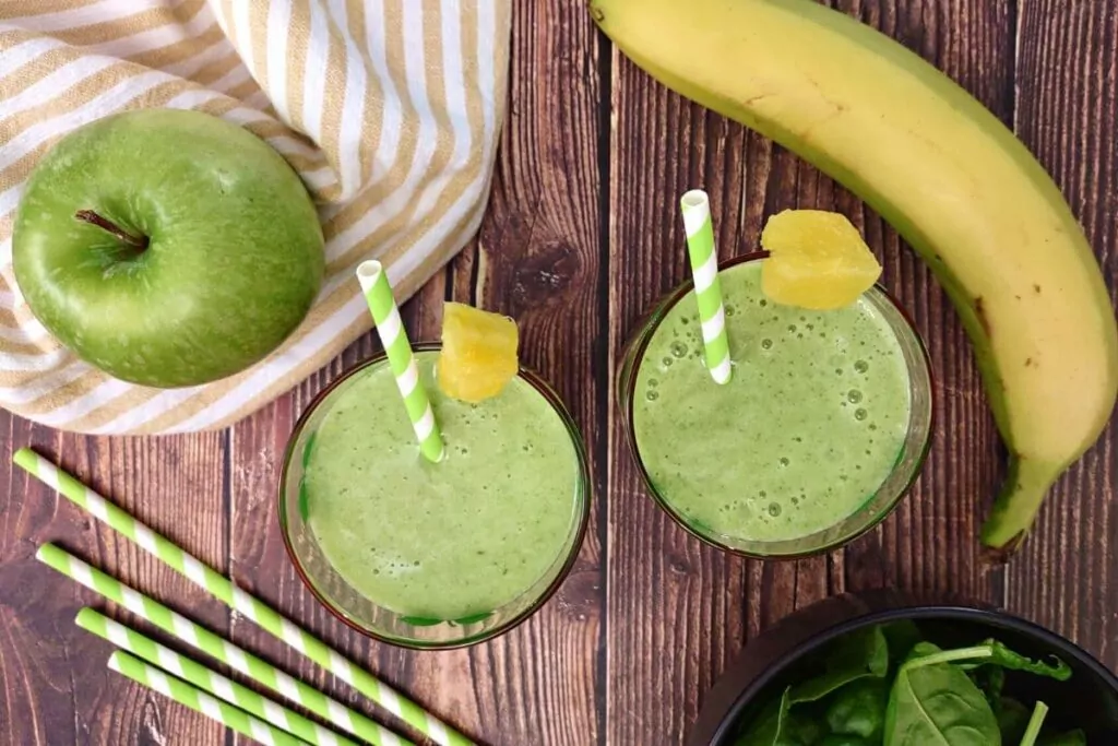 overhead view of pineapple green apple smoothie drinks in a glass with fresh fruit