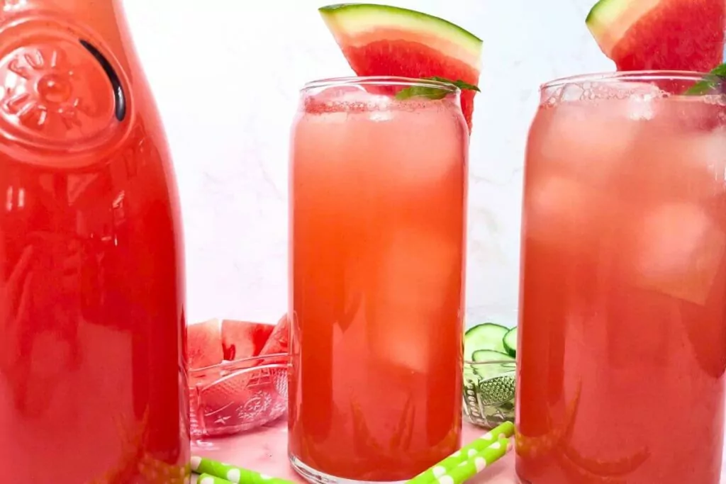 two tall glasses of cold watermelon cucumber agua fresca next to a pitcher