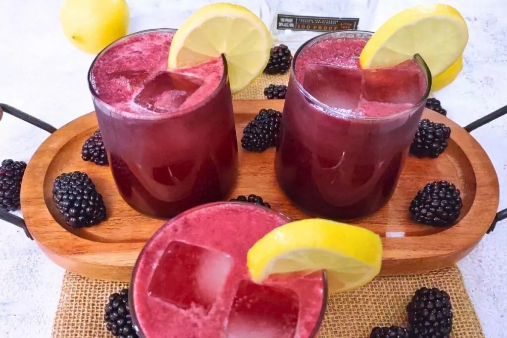 3 glasses of bourbon blackberry lemonade on a wooden serving platter