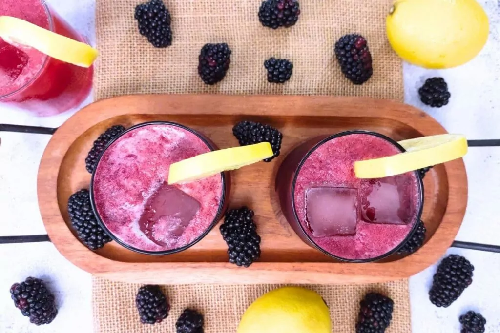 overhead view of bourbon blackberry lemonade on a wooden serving tray with fresh fruit