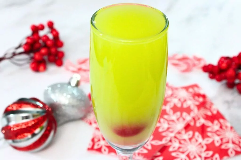grinch mimosa cocktail surrounded by festive christmas decorations