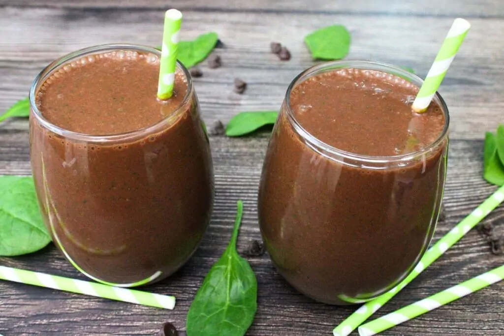 two glasses filled with chocolate peanut butter spinach smoothies and paper straws