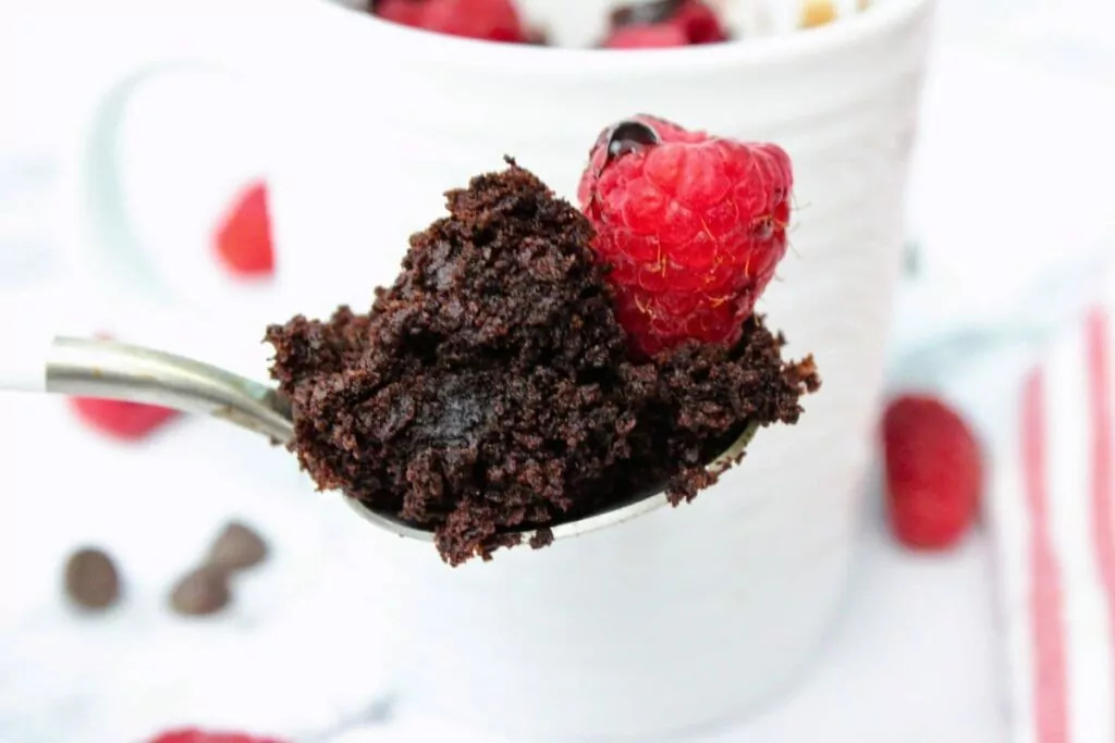holding up a spoonful of chocolate raspberry mug cake with a fresh raspberry