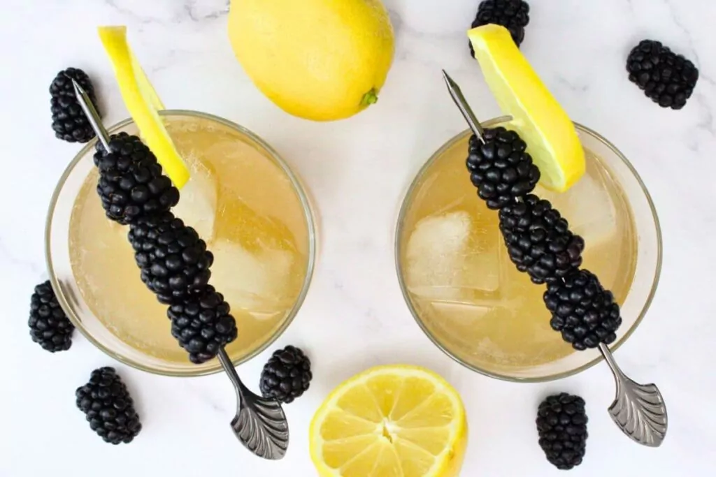 overhead view of two crown royal blackberry whiskey sour drinks with fresh fruit surrounding