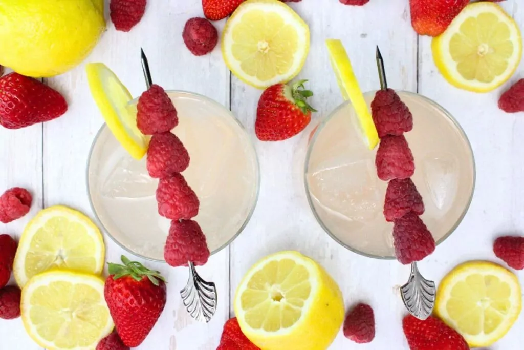 overhead view of two gin and pink lemonade cocktails with raspberry skewers