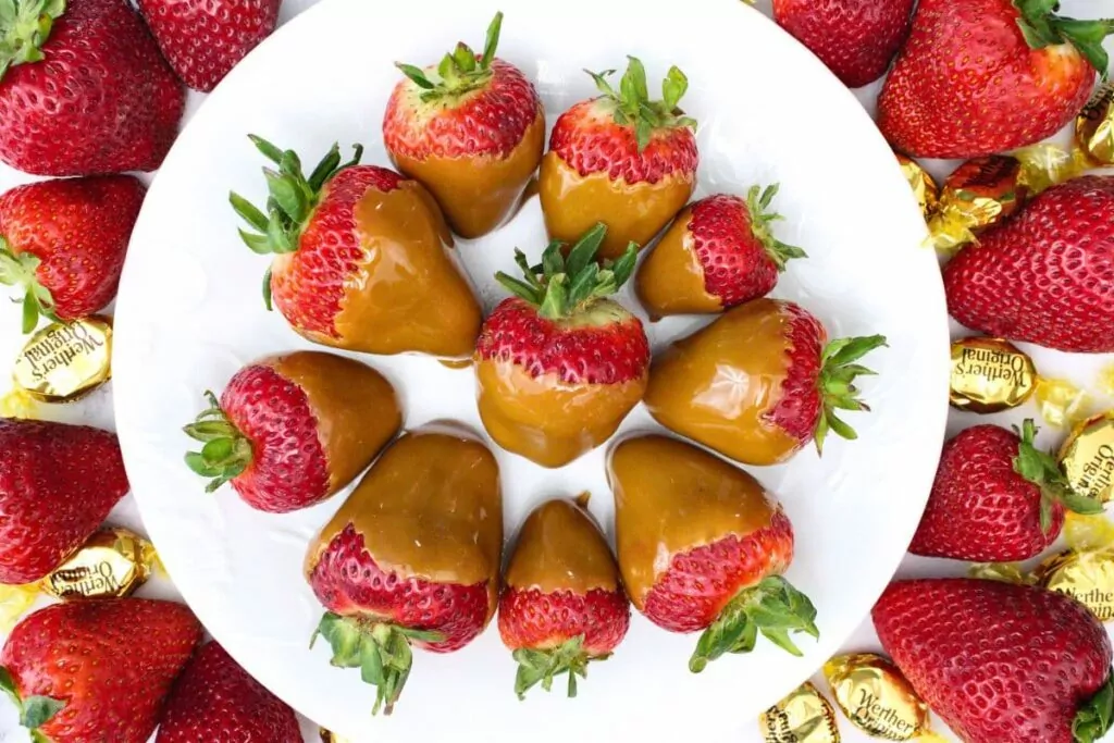 overhead view of several caramel candied coated strawberries circling a plate
