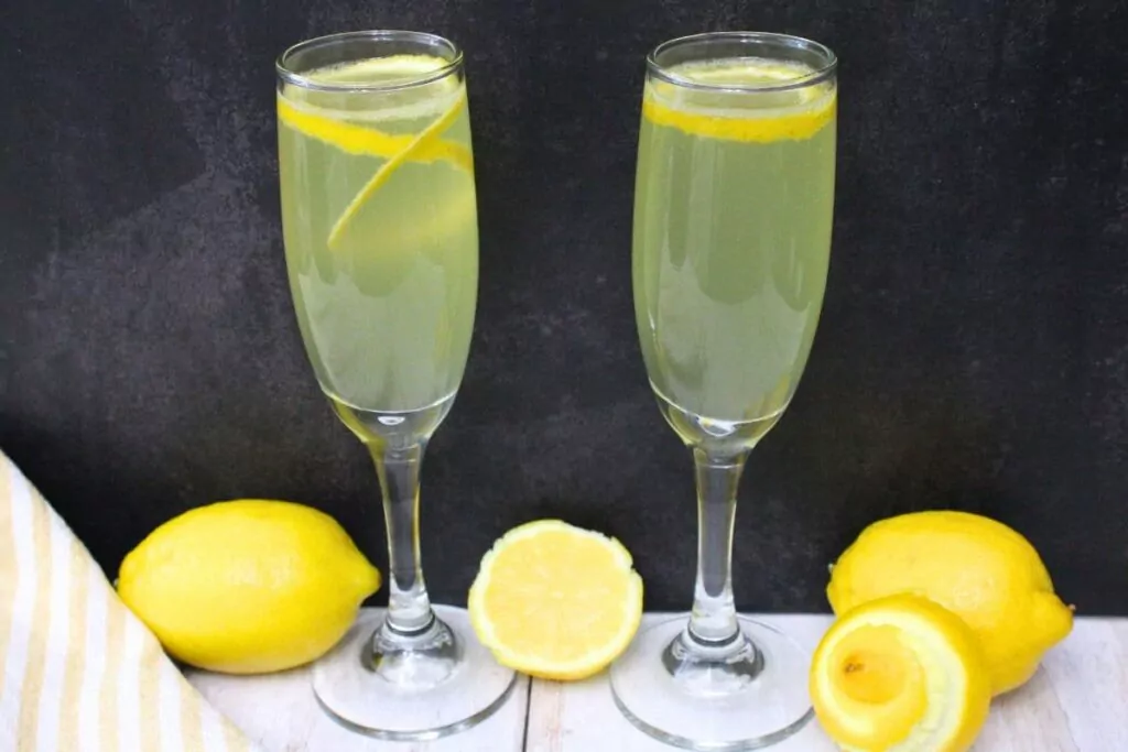 two champagne flutes filled with limoncello french 75 cocktail against a dark background