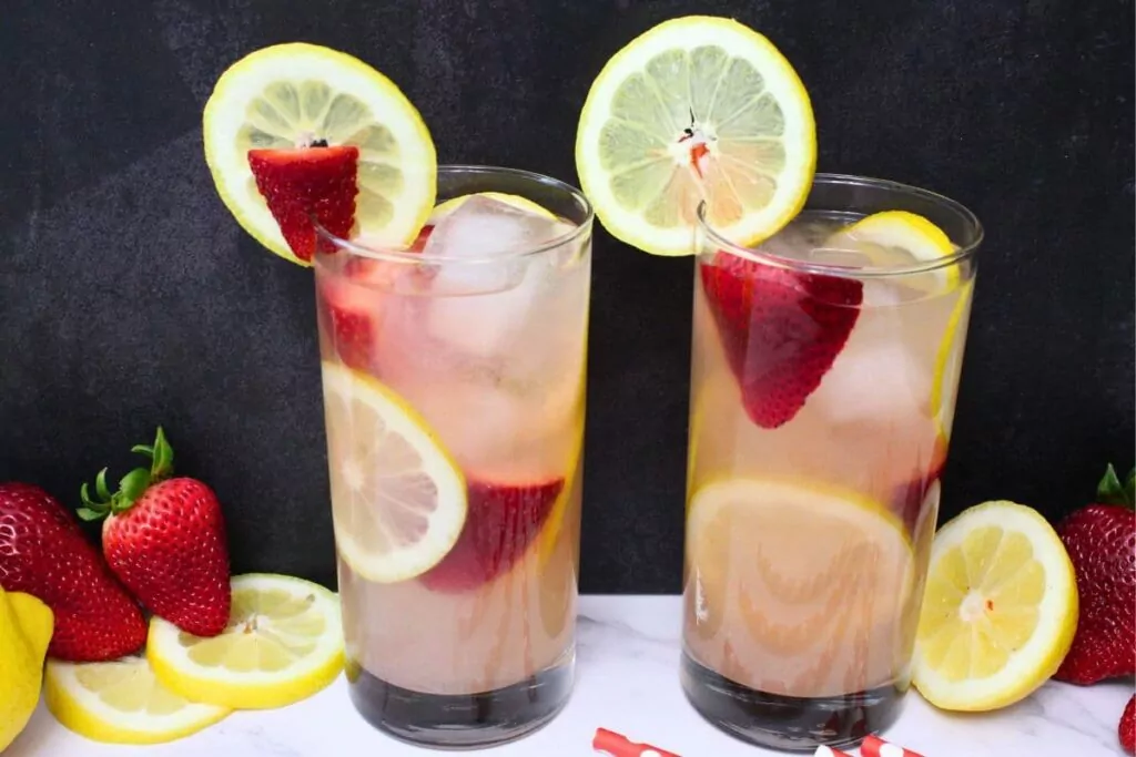 two strawberry vodka lemonade cocktails with fresh fruit in the rim
