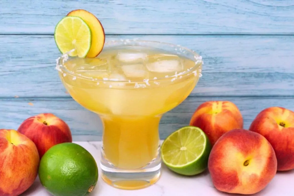 crown peach margarita against a blue wood background surrounded by fresh fruit