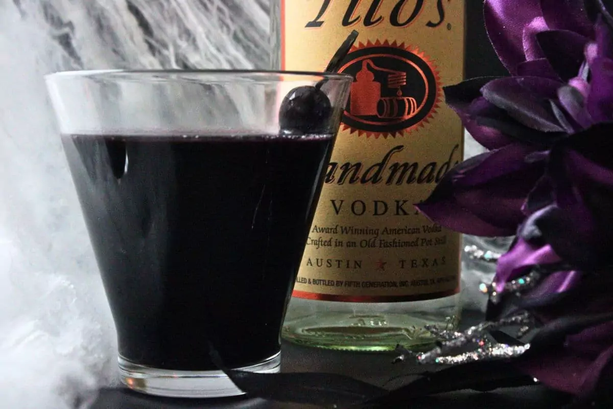 closeup side view of black martini drink in front of vodka bottle