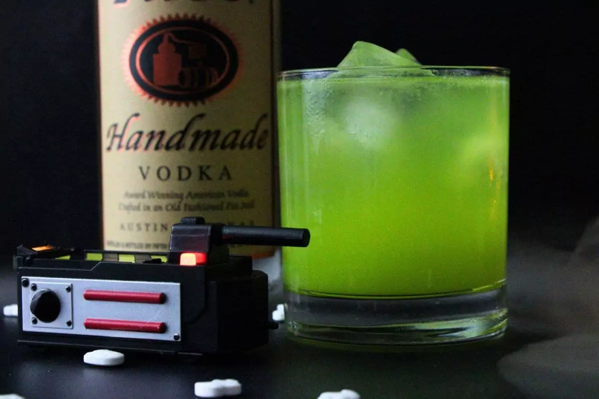 closeup side view of ghostbusters cocktail next to ghost trap and vodka bottle