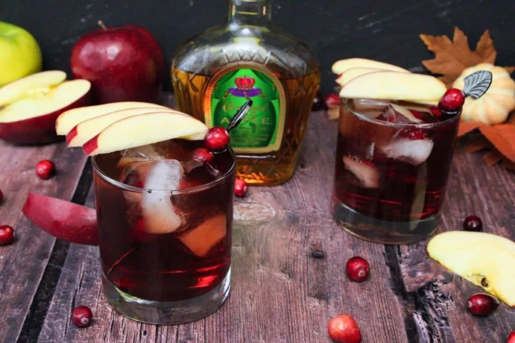 two crownberry apple drinks with fresh apple slices in front of crown royal apple bottle