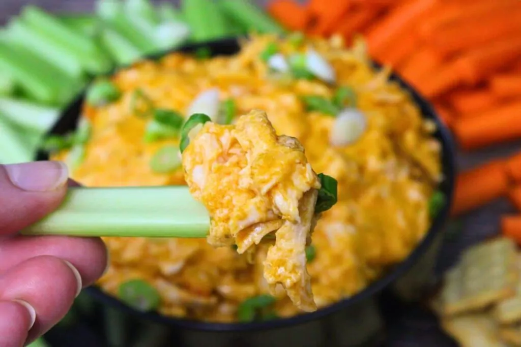 holding up a piece of celery loaded with buffalo chicken dip