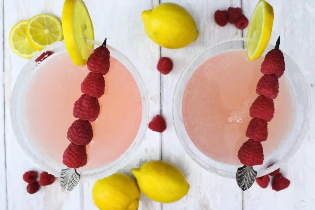overhead view of two pink lemon drop martini drinks with a skewer of raspberries