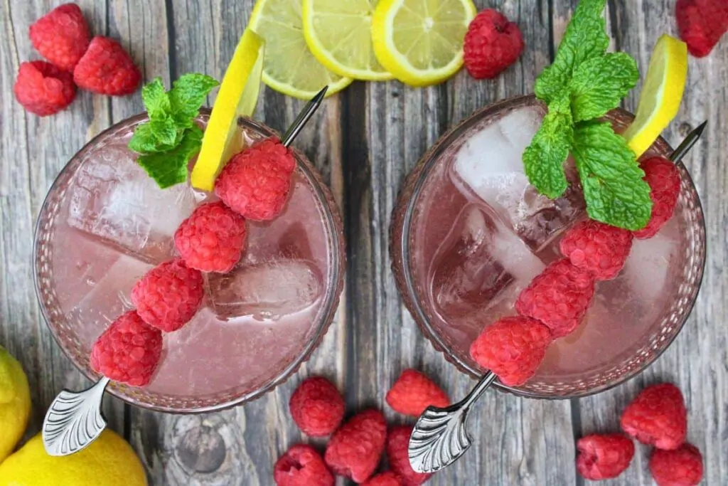 overhead view of two gin and jam cocktails garnished with raspberry skewer and lemon slice on a wooden table