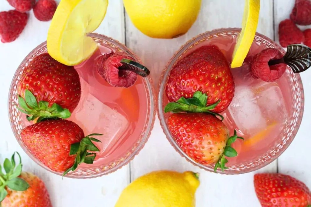 overhead view of two glasses of pink whitney jungle juice garnished with lemon, strawberry, and raspberry