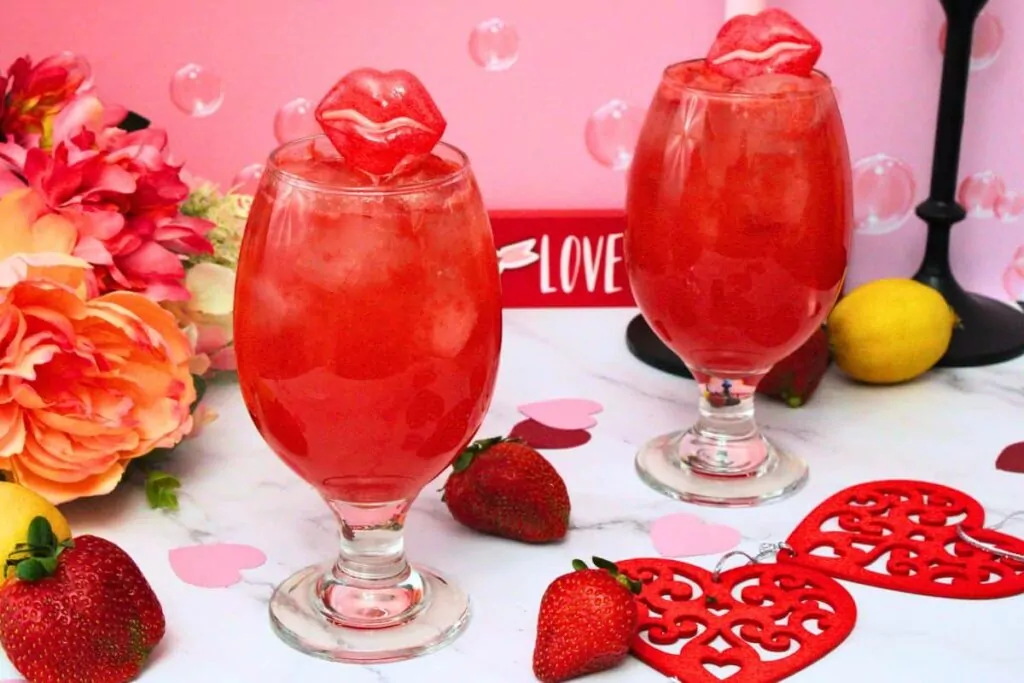 two applebees tipsy cupid cocktails against a pink background surrounded by hearts, flowers, and fresh fruit